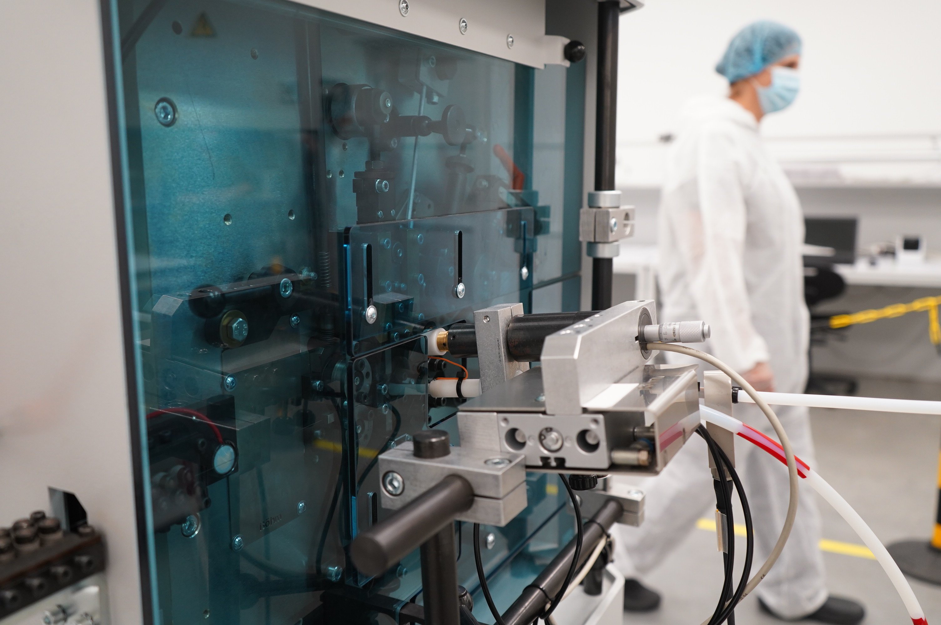 Close-up of automated medical production equipment with a technician working in a cleanroom.
