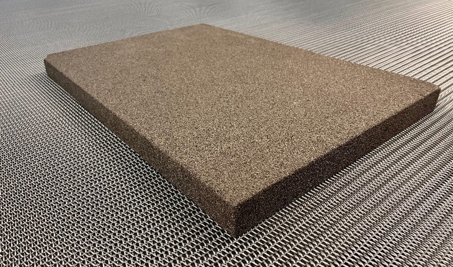 Eine rechteckige braune Verbundplatte mit strukturierter Oberfläche liegt auf einem geriffelten Metallboden und vermittelt ein modernes und industrielles Gefühl.