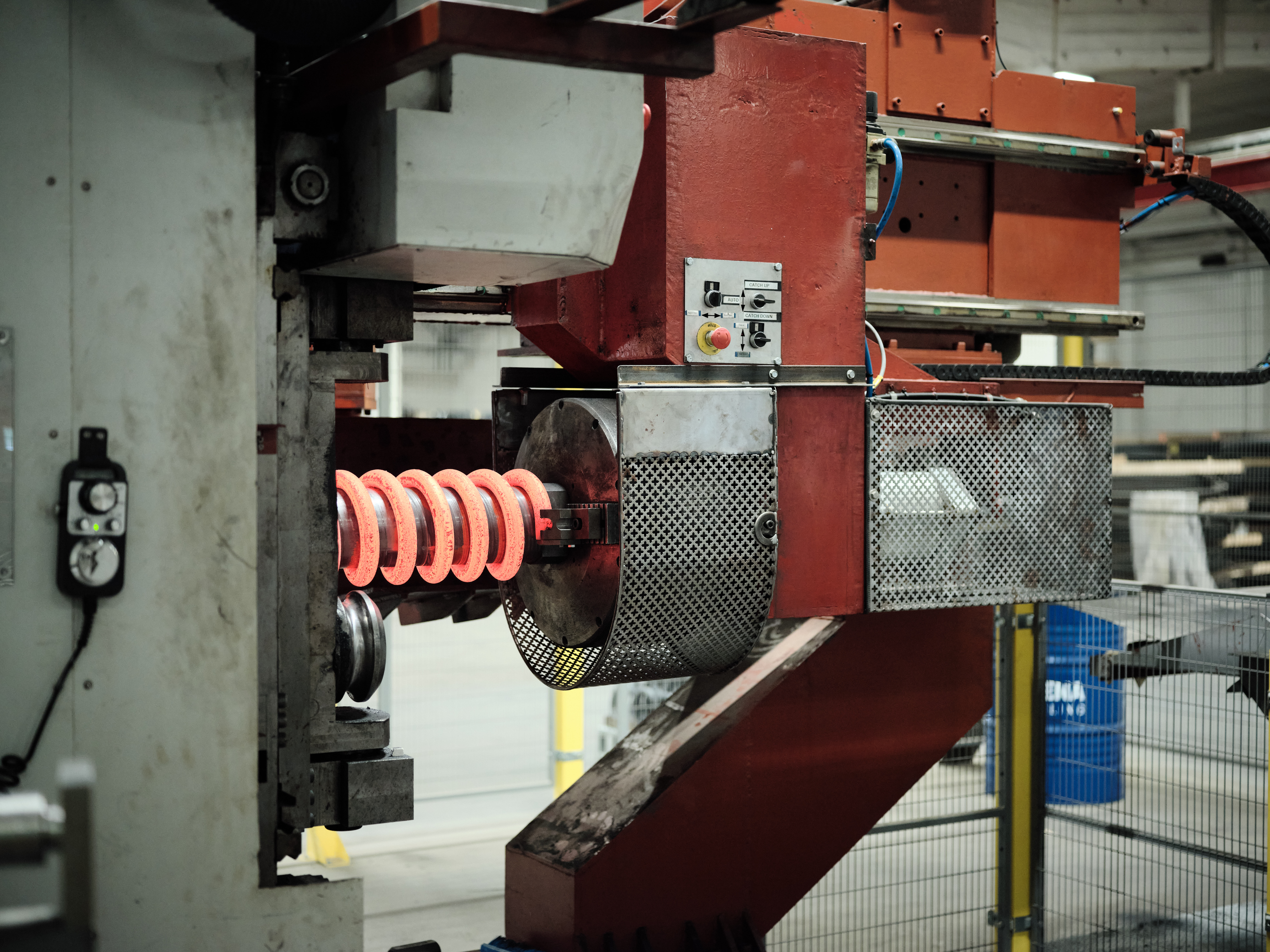 En glødende rød trykfjeder formes omkring en metalcylinder i en produktionsmaskine.