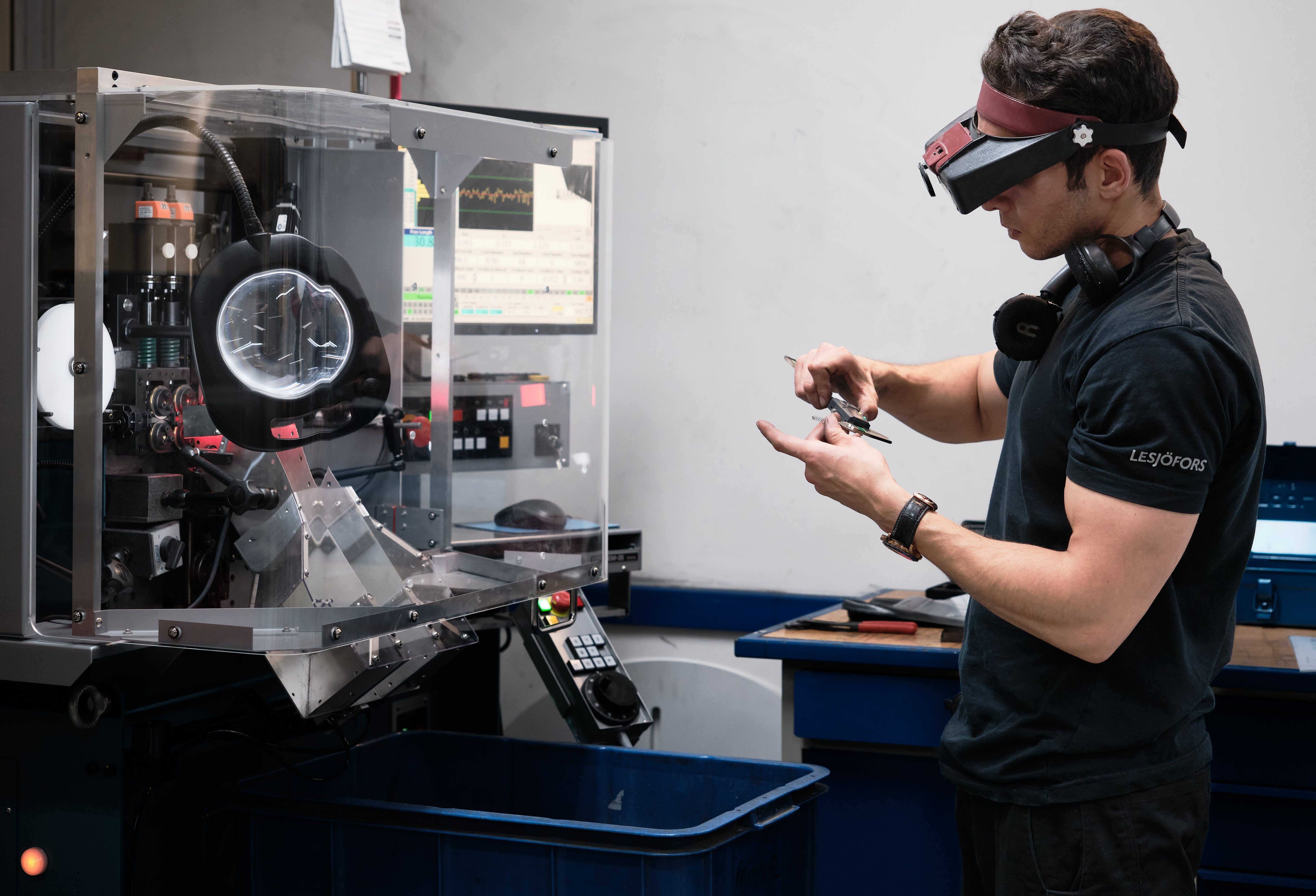 Tekniker mäter en liten metallkomponent bredvid en CNC-lindningsmaskin.