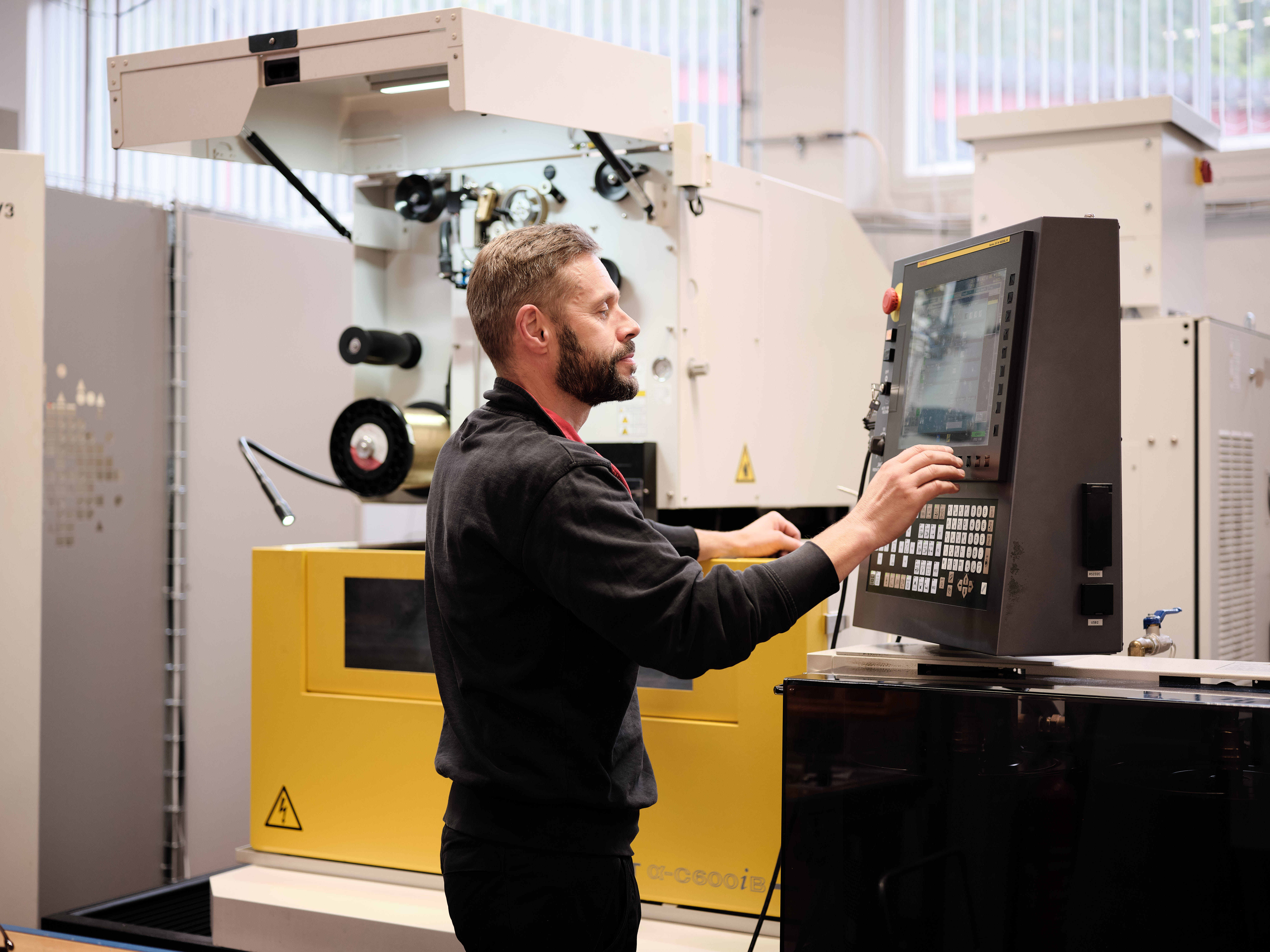 En fabriksarbejder betjener en CNC-maskine via et kontrolpanel i et værksted.