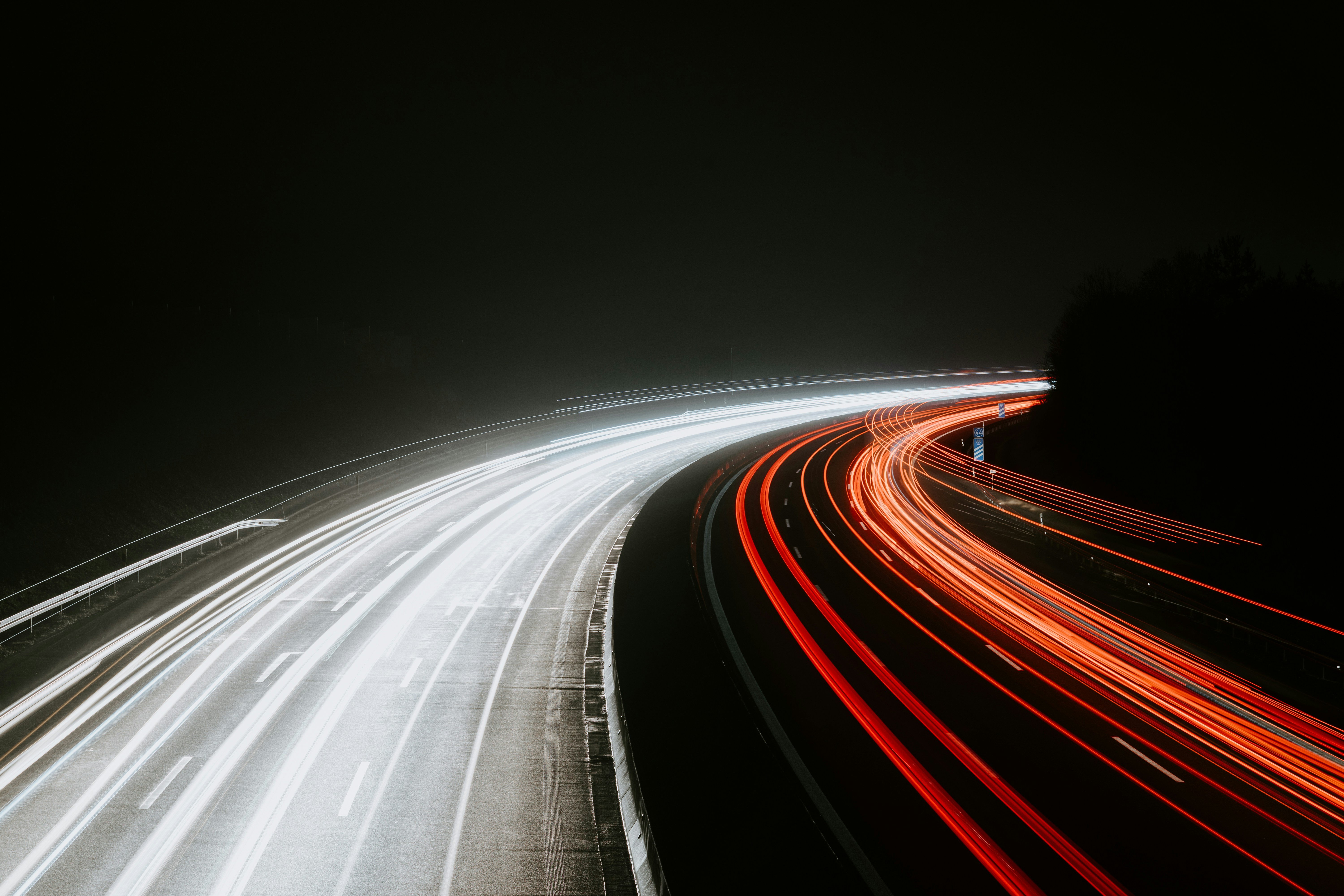 Weiße und rote Lichtspuren des Verkehrs auf einer kurvigen Autobahn bei Nacht.