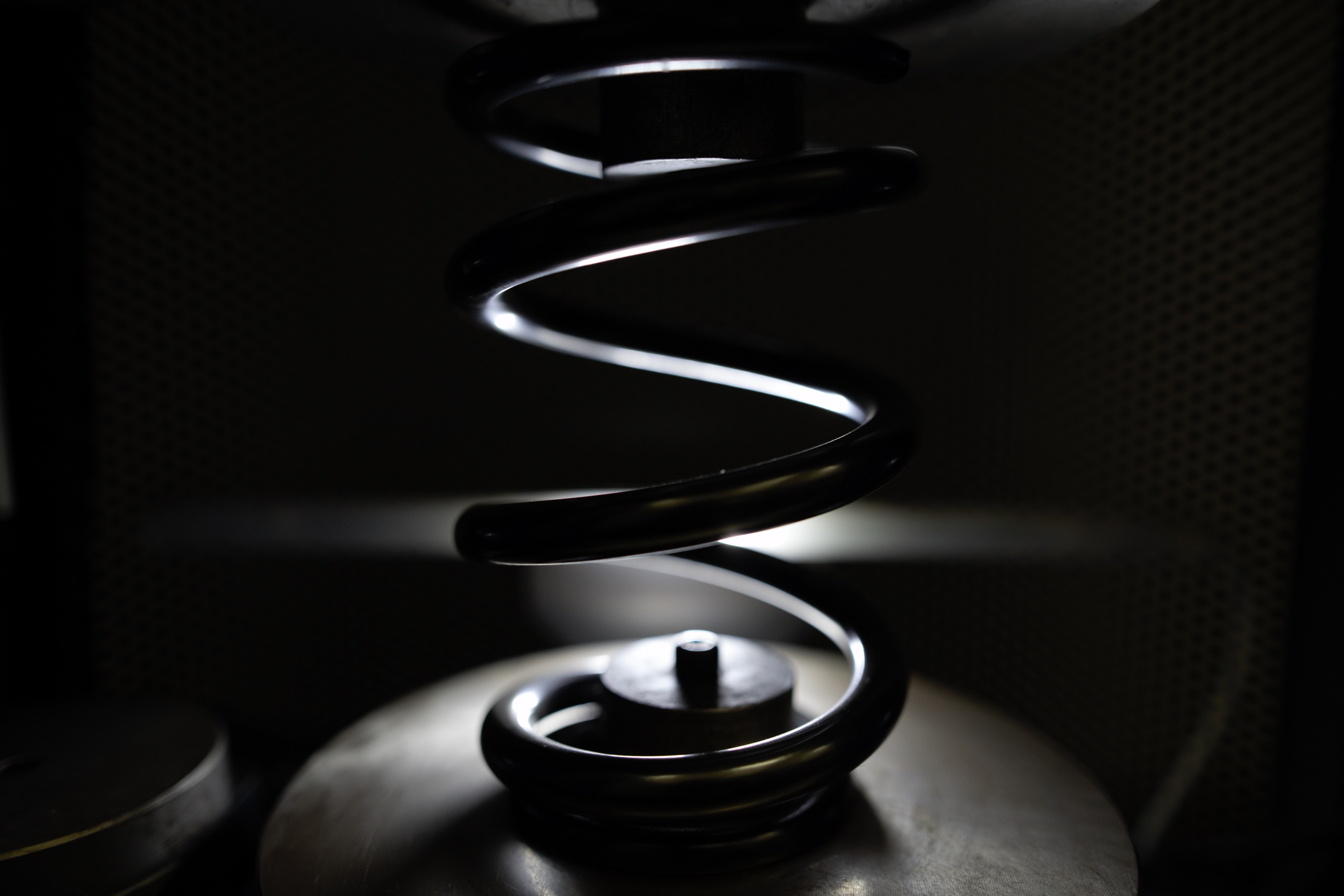 Spiralfjäder i metall under en 3D-optisk mät- och testskanner, belyst mot en mörk bakgrund.