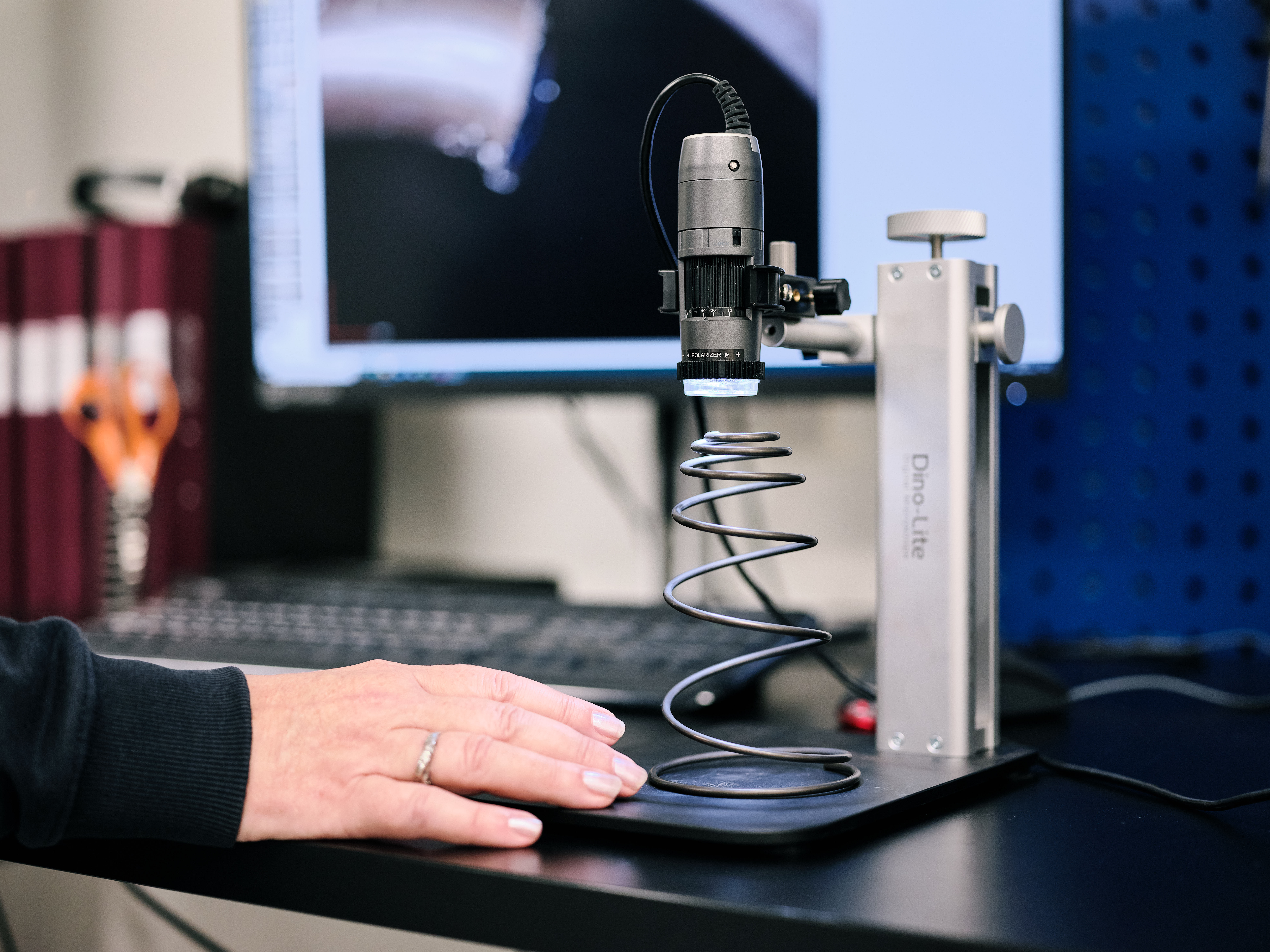 Techniker prüft eine konische Druckfeder unter einem Mikroskop an einem Arbeitsplatz.
