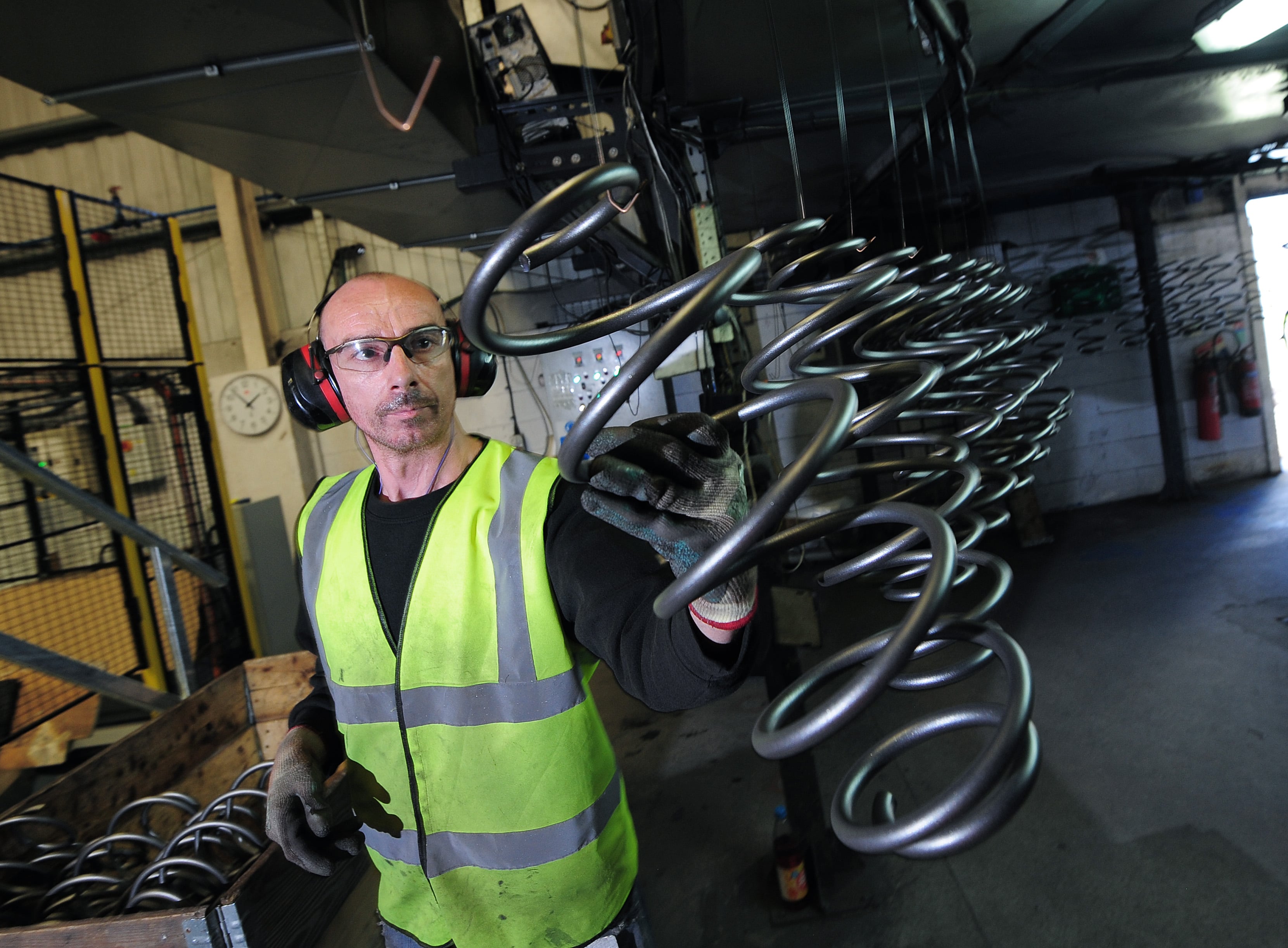 En fabriksarbejder iført sikkerhedsudstyr inspicerer store metalspiraler med et fokuseret udtryk.