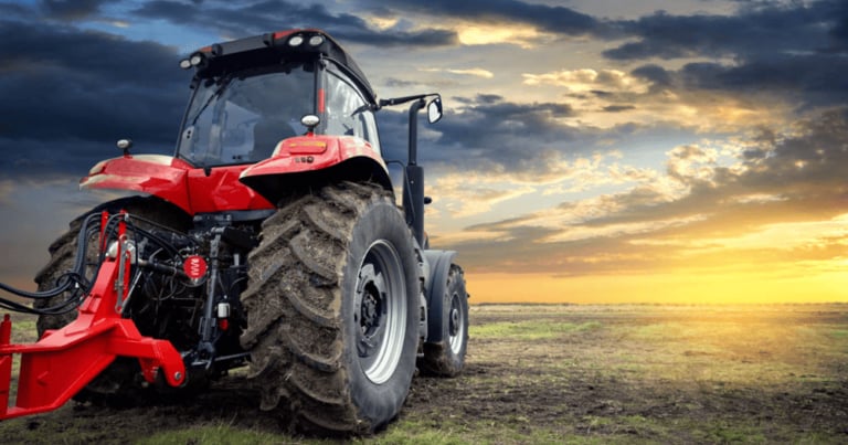 Ein roter Traktor mit großen Reifen steht auf einer Wiese unter einem dramatischen Sonnenuntergang.