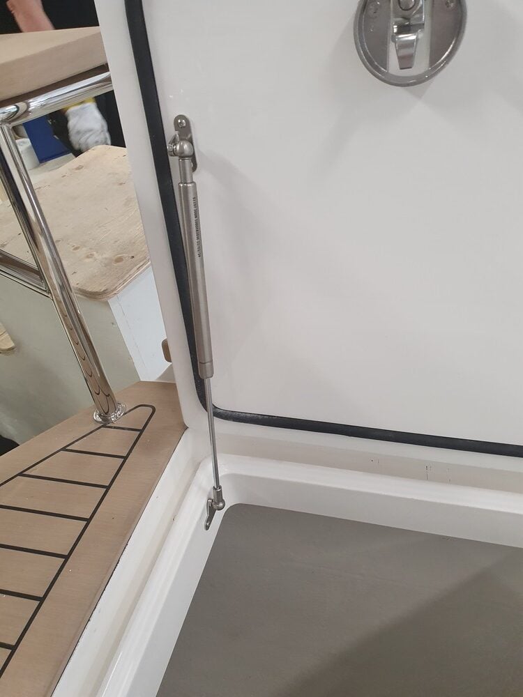 Stainless steel gas spring mounted on a marine hatch, holding the compartment lid open.