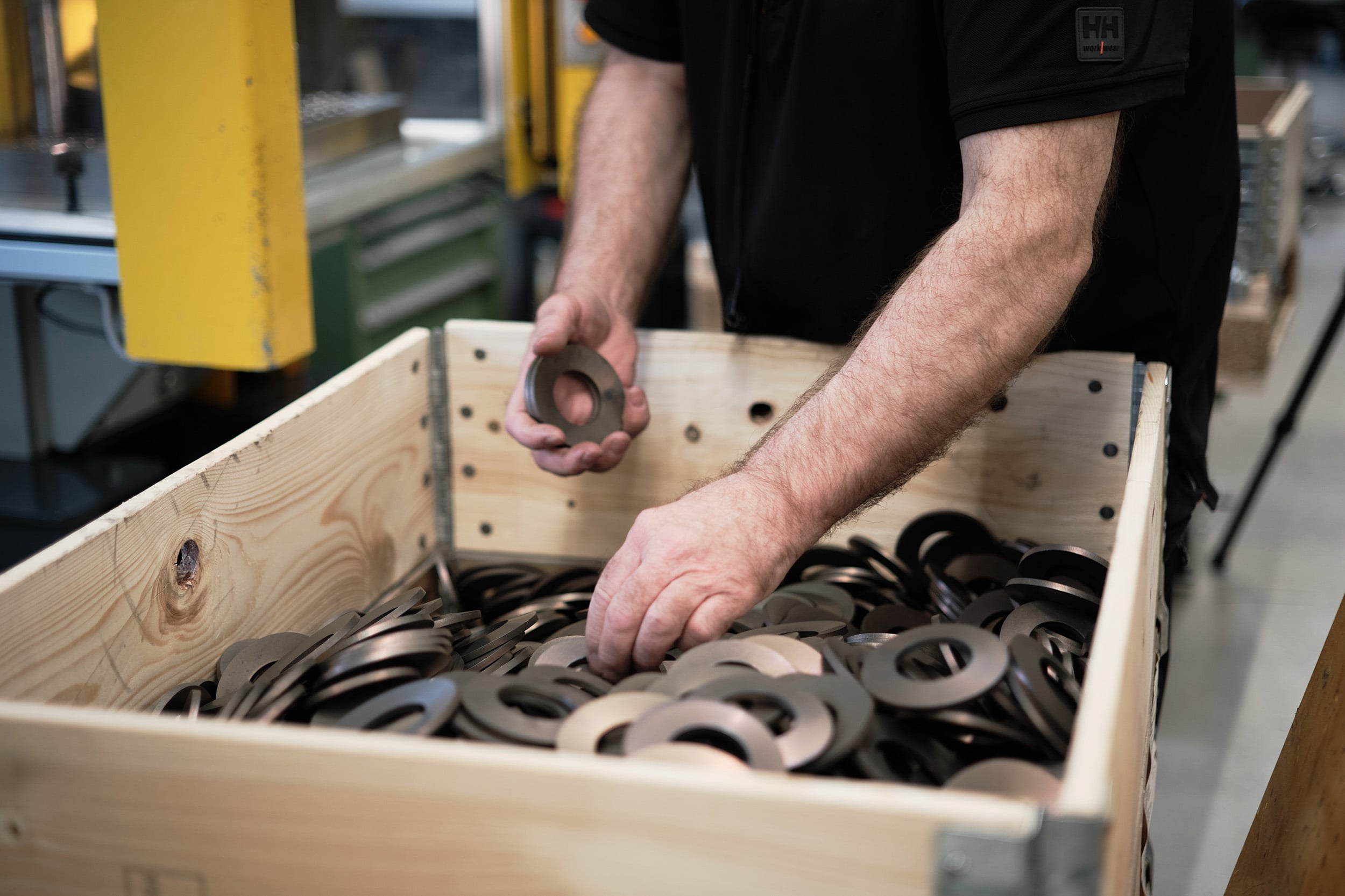 Employee inspecting precision metal disc springs in a wooden crate inside a Lesjöfors manufacturing facility before the next stage of production.