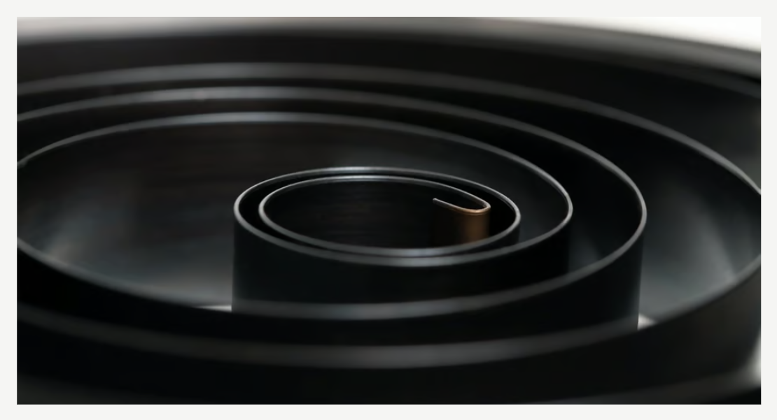 A black, single coiled spiral torsion spring.