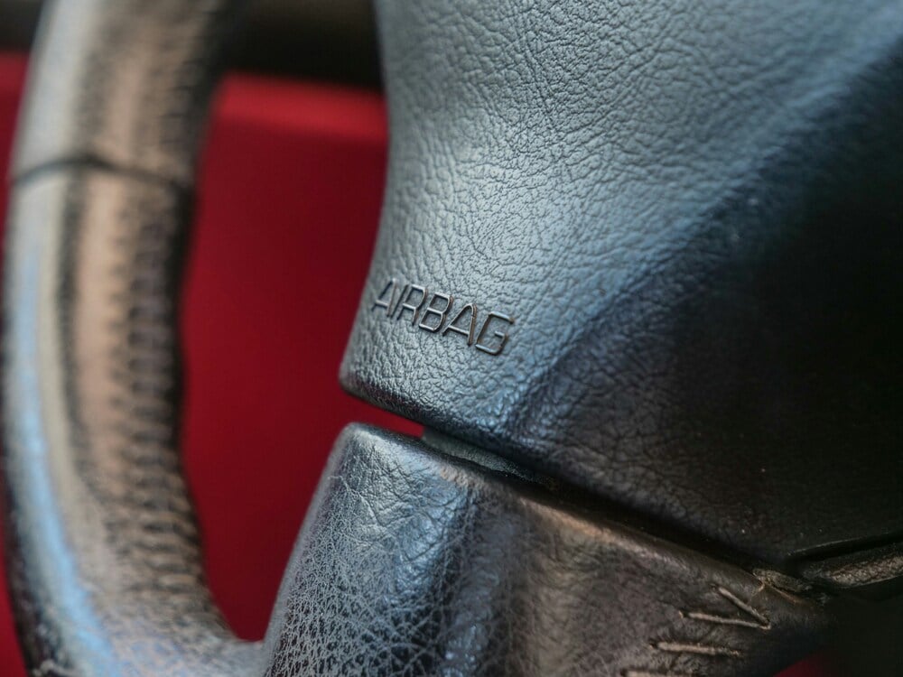 Close-up of a steering wheel's center airbag module, marked "airbag" – the driver's airbag connects through the clock spring behind it 
