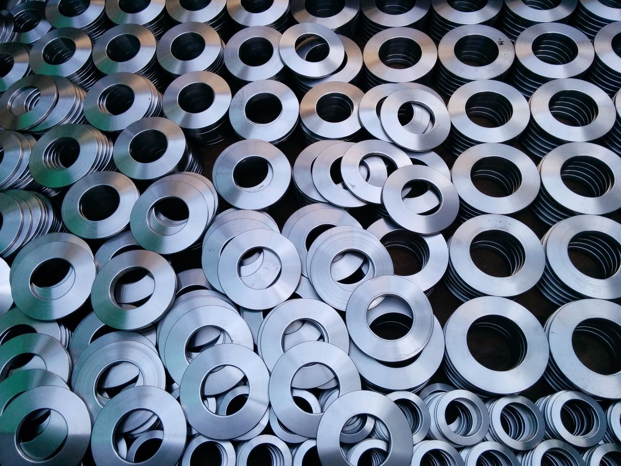 Large batch of steel disc springs in various diameters, stacked and loosely arranged after manufacturing.