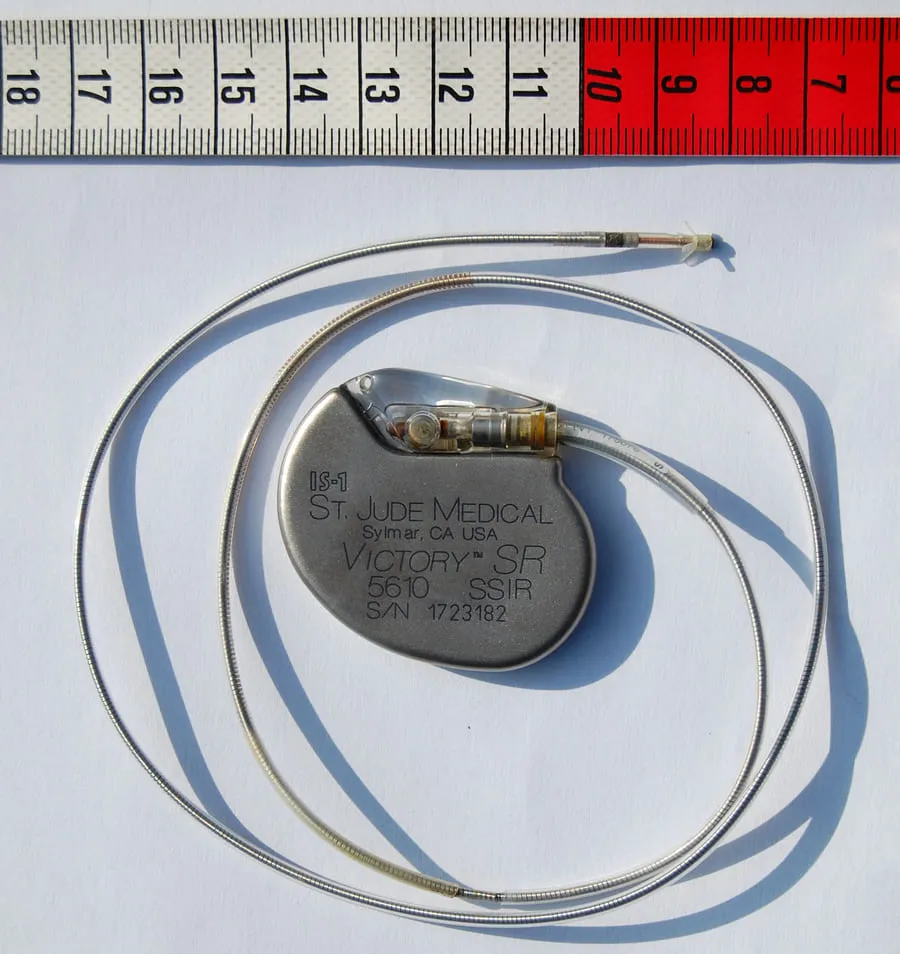 Implantable cardiac pacemaker with leads placed next to a measuring ruler.