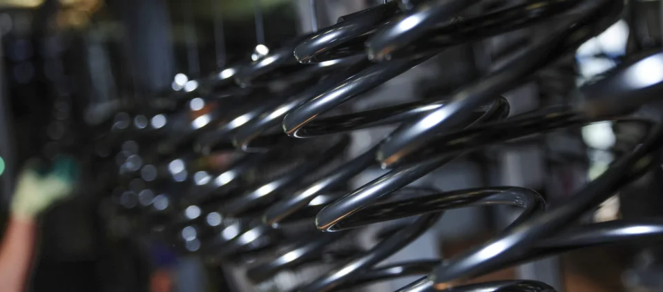 Close-up of black metal coil suspension springs in a manufacturing setting.