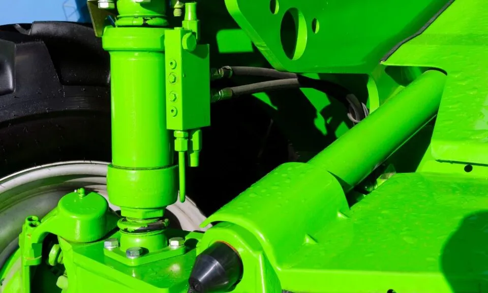 Nærbilde av en klart grønn hydraulisk mekanisme med bolter og rør mot en mørk dekkbakgrunn.