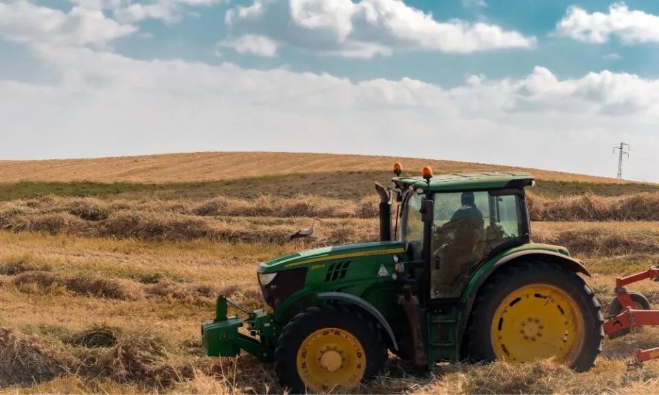 En grønn traktor står i en gyllen hveteåker under en skyet himmel.