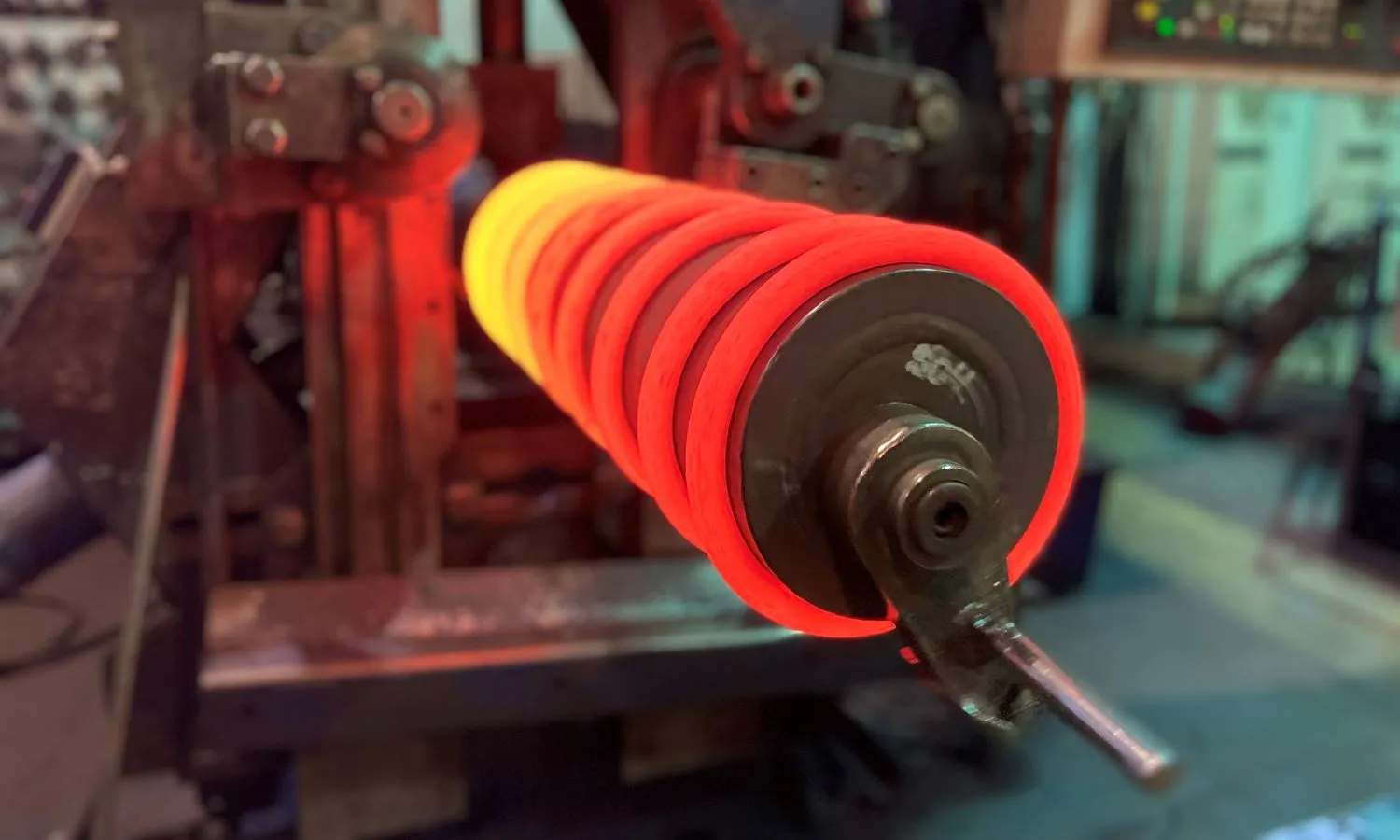 Ein glühend orangeheißes zylindrisches Metallobjekt befindet sich rechts, umgeben von Industriemaschinen bei gedämpfter Beleuchtung.