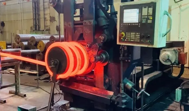 Glühend heißer Stahldraht wird auf einer robusten industriellen Warmwickelmaschine in einer Produktionsanlage zu einer Federform gewickelt.