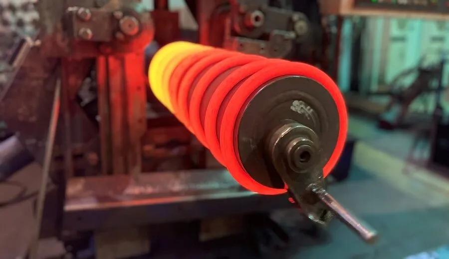 Makroaufnahme einer glühend rot-orangen warmumformten Druckfeder auf einem Dorn während des Warmumformungsprozesses.