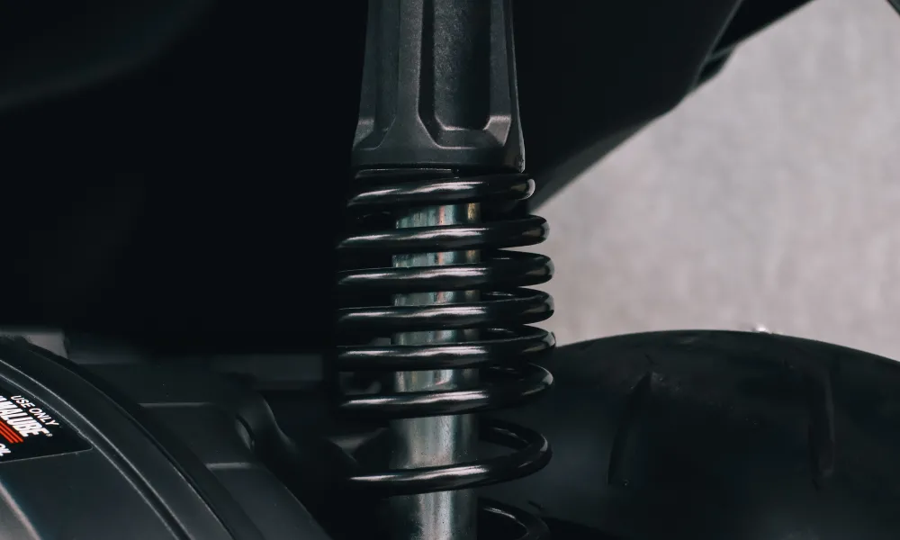 Close-up of a black compression spring around a shock absorber in a vehicle suspension system.