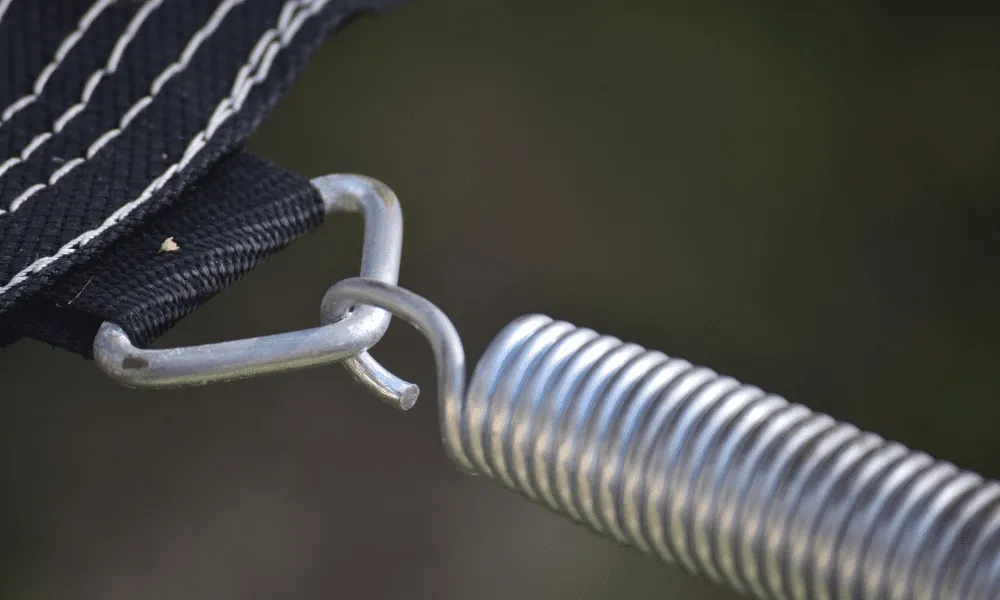 Nærbilde av en metallkrok koblet til en spiralfjær, festet til en svart trampoline.