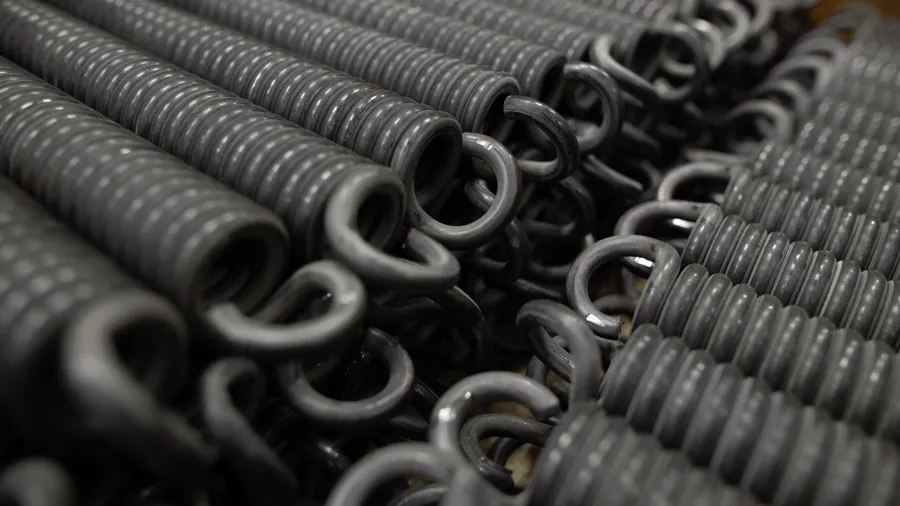 Nahaufnahme von eng gewickelten schwarzen Metallfedern, die horizontal aufgereiht sind. Ihre glänzende Oberfläche lässt auf Haltbarkeit und Stärke schließen.