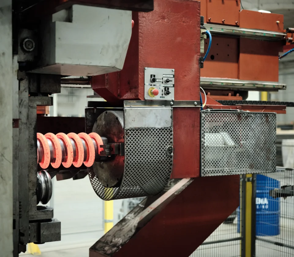 Heated metal rod being formed into a coil spring by industrial machinery.