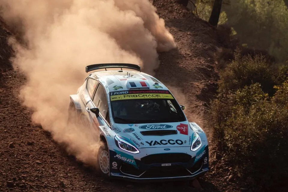 Rally car racing on a dirt track, kicking up dust during high-speed cornering.
