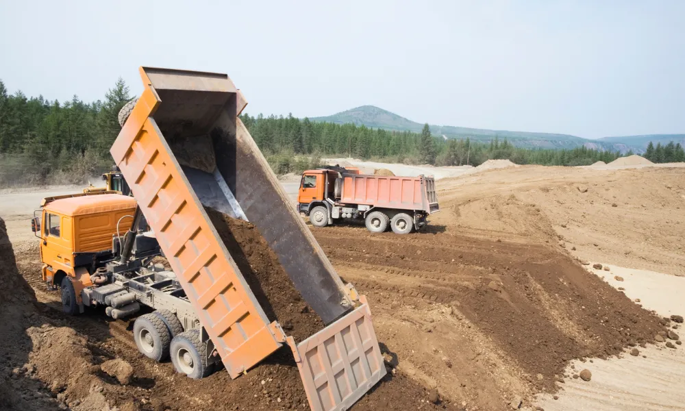 Orangefarbene Lastwagen laden Erde und Bodenmaterial auf einer Baustelle oder in einem Steinbruch unter freiem Himmel ab.