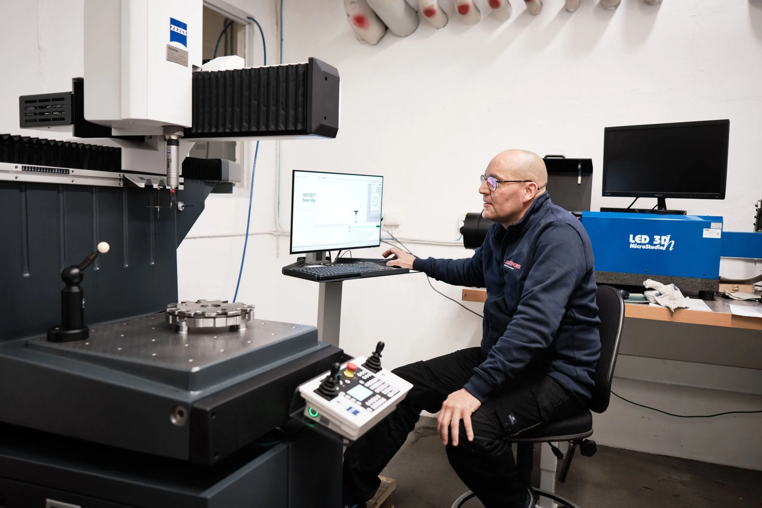 Technician seated at a coordinate measuring machine, analyzing a metal component on a computer screen.