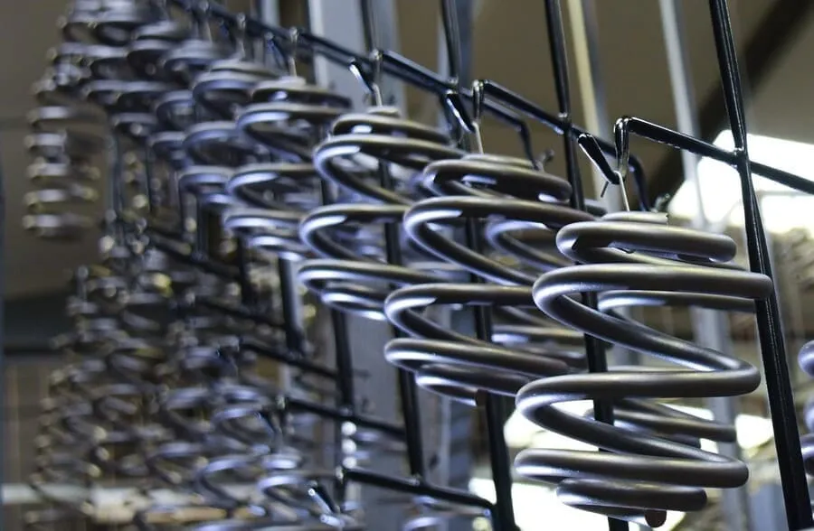 Close-up of multiple coiled suspension springs hanging from a rack on a powder coating production line in a manufacturing facility.