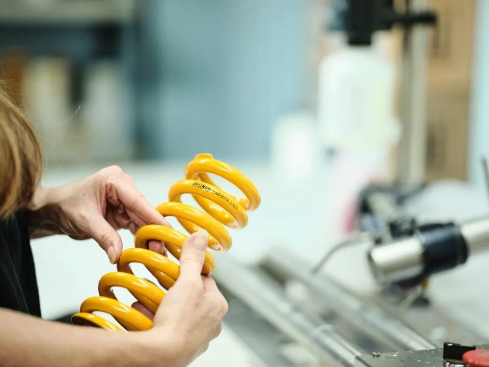 Technician inspecting a yellow coil spring in a manufacturing or testing environment.