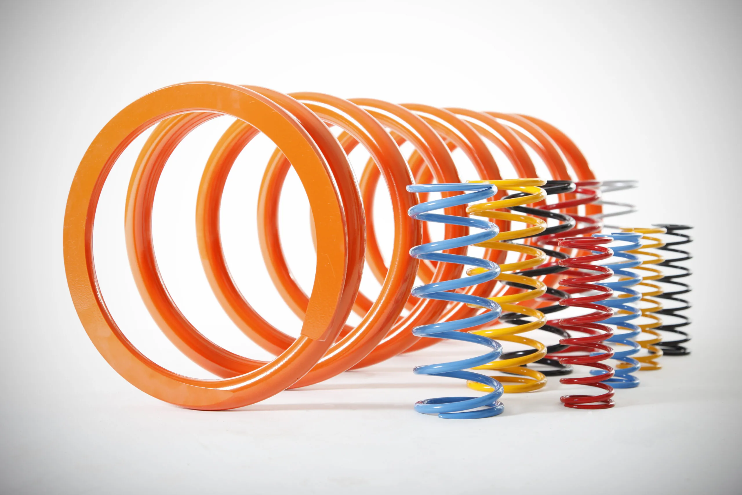 A collection of powder-coated coil springs in various sizes and colours including orange, blue, yellow, red, black, and silver, arranged together against a white background.