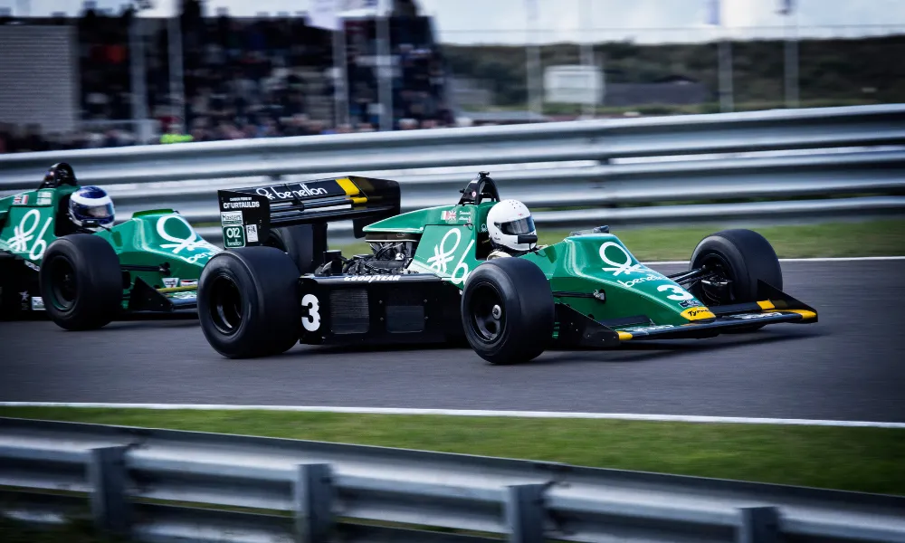 Zwei Benetton-gesponserte Vintage-Formel-1-Wagen fahren ein Rennen auf der Strecke, der Führende trägt die Startnummer 3 in grün-schwarzer Lackierung.
