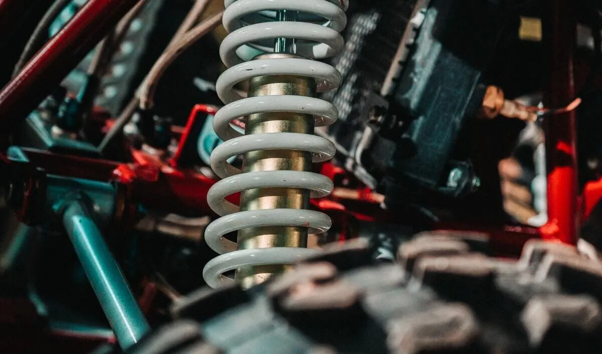 Nahaufnahme einer weißen Schraubenfeder in einer mechanischen Umgebung, umgeben von Metallstangen und Drähten.