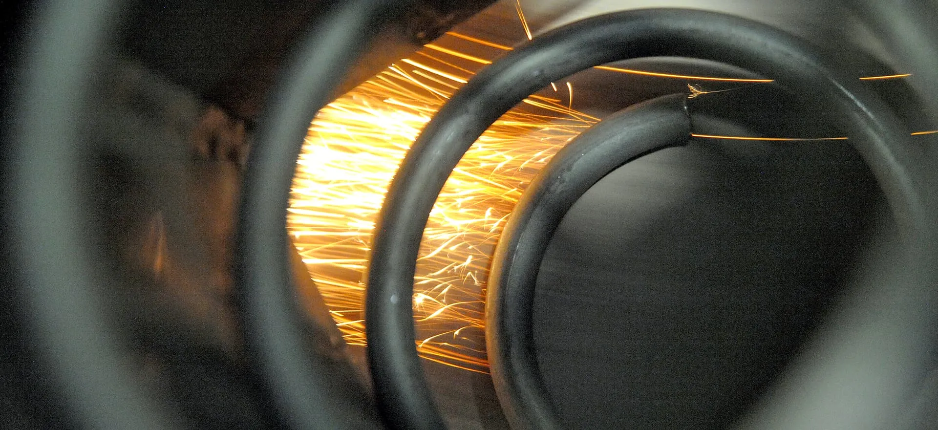 Close up image showing a coiled material and sparks as a stainless steel spring is manufactured.