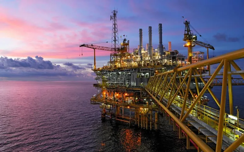 Offshore oil and gas platform with industrial structures and pipelines at sunset over the ocean.