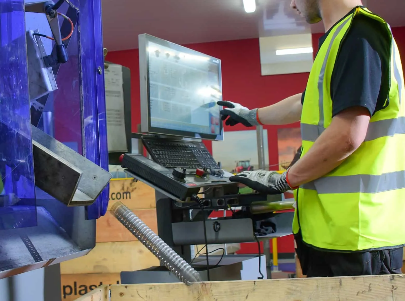 Factory worker in high-visibility vest operating a touchscreen control panel on industrial machinery.