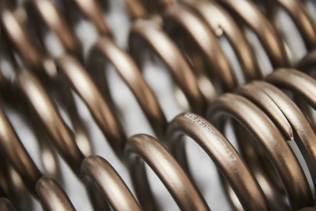 Nahaufnahme bronzefarbener Metall-Spiralfedern in einer Reihe, mit dem Markennamen Lesjöfors auf der Oberfläche.