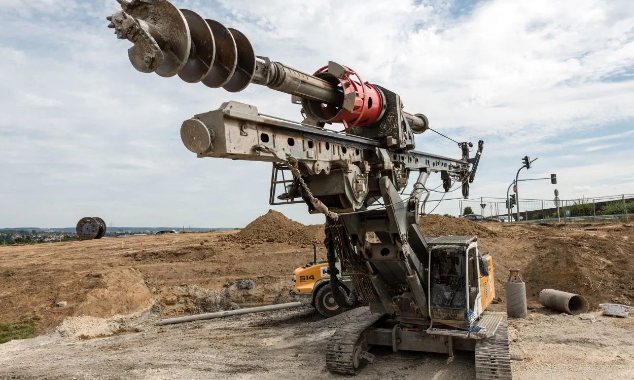 Large tracked drilling rig with an extended auger bit operating on a construction site.