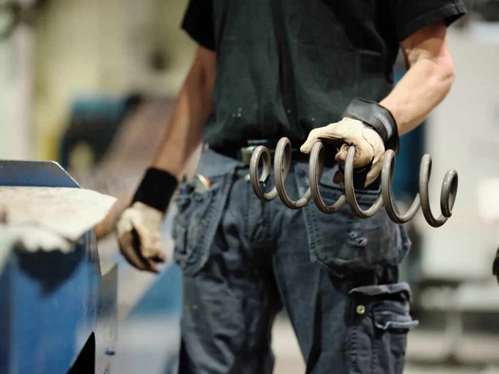 Ein Lesjöfors-Fabrikmitarbeiter mit Handschuhen hält ein Set Bananenfedern in einer industriellen Fertigungsumgebung.