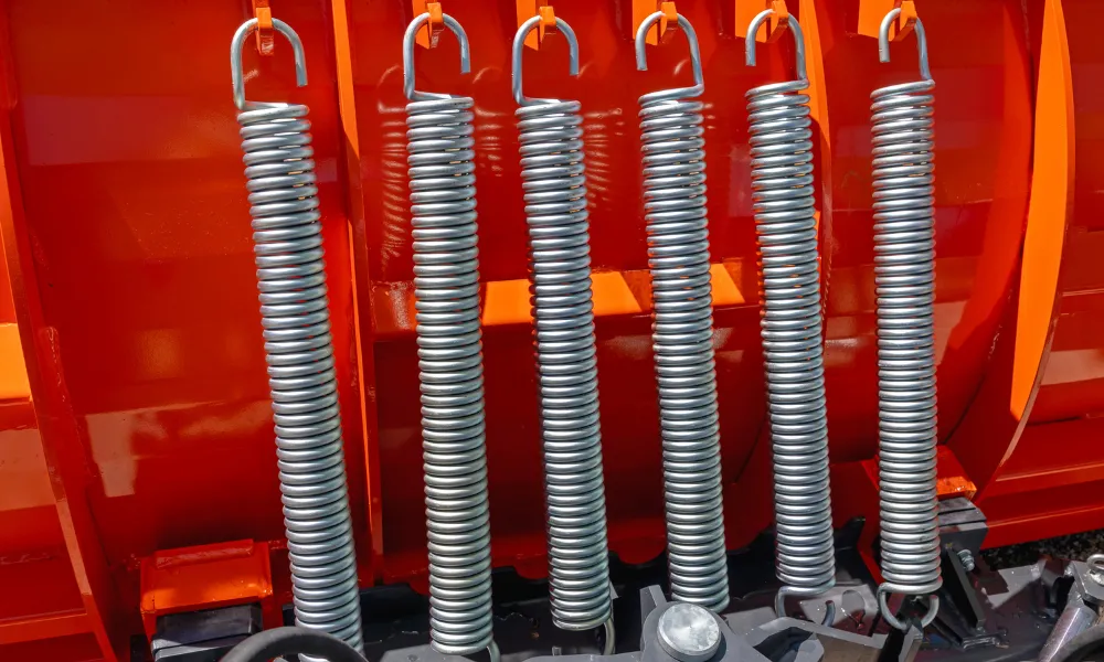 Row of five galvanized steel tension springs with hook ends, mounted vertically on red agricultural machinery.