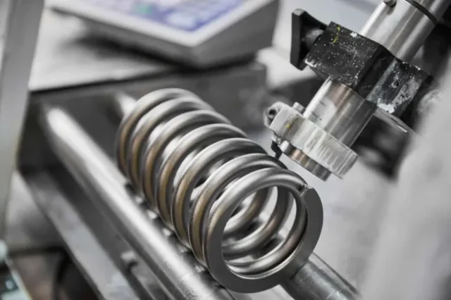 Detailed view of a compression spring on a testing rig, with a measuring probe inspecting it.