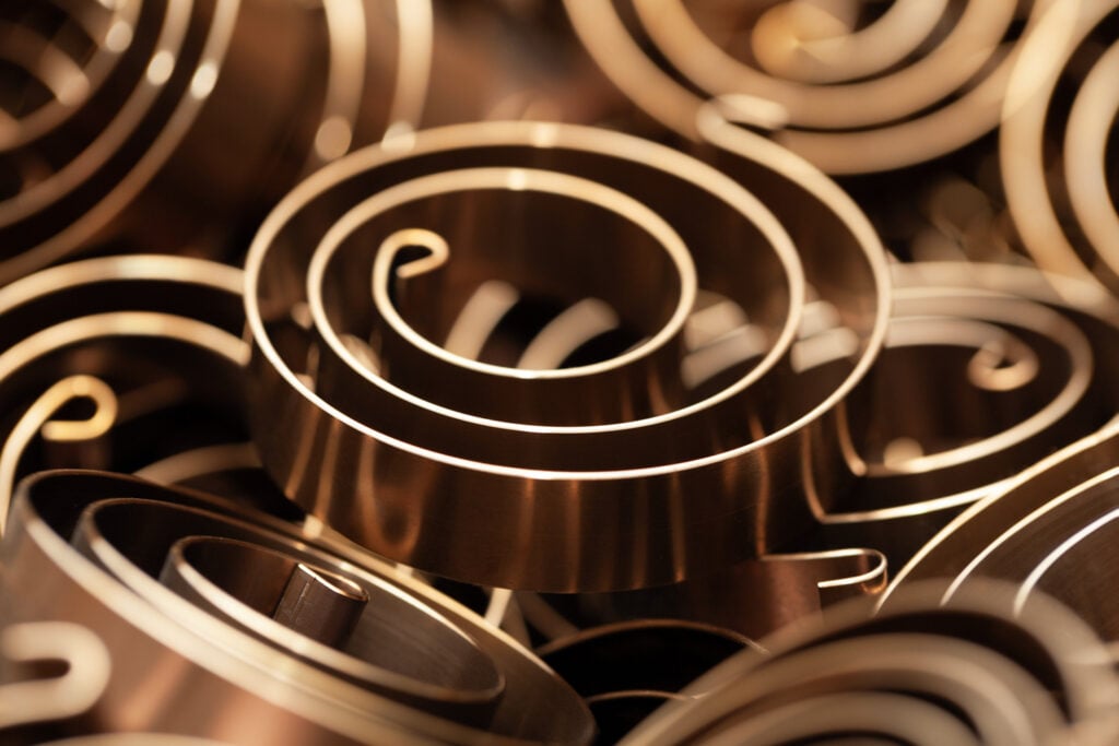 Nahaufnahme von bronzefarbenen Torsionsspiralfedern, kunstvoll geschichtet, sodass ein Muster aus Kreisen und Spiralen entsteht.