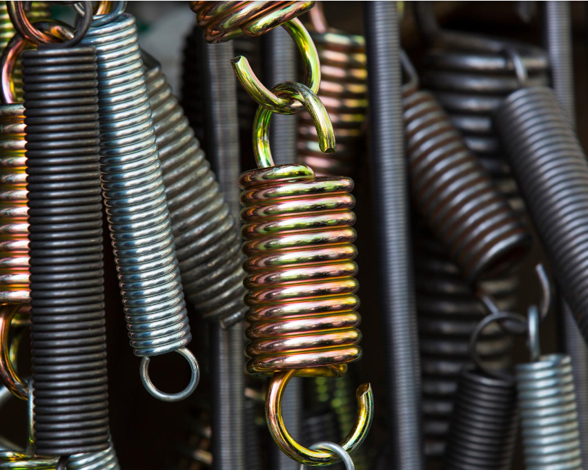 Nahaufnahme verschiedener Metallfedern, die vertikal angeordnet sind und unterschiedliche Größen und Farben zeigen. Das Bild betont industrielle, mechanische Texturen.