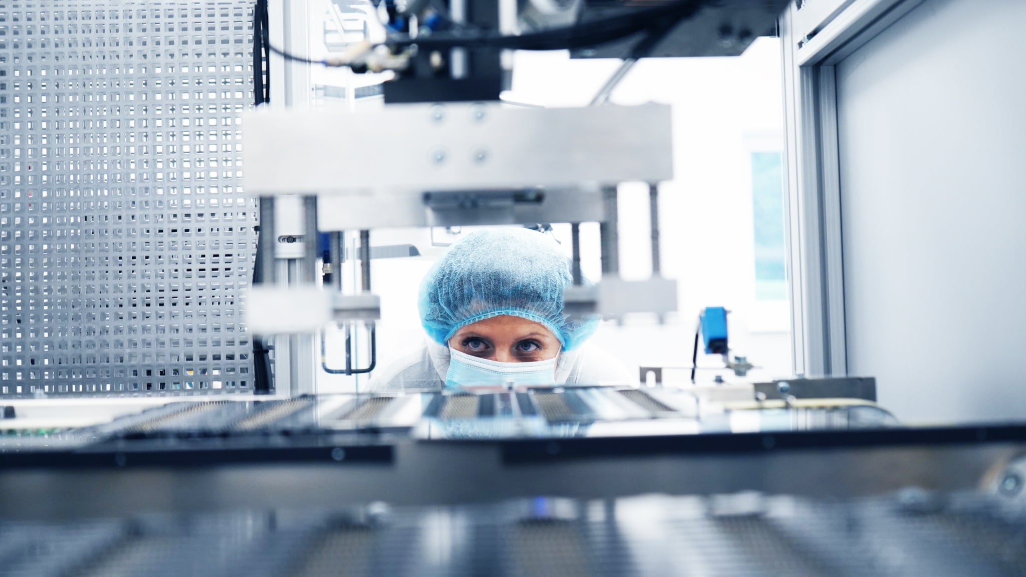 Eine Person mit blauem Haarnetz und Gesichtsmaske konzentriert sich intensiv auf Maschinen in einem sterilen Labor und vermittelt Präzision und Konzentration in einer hochtechnologischen Umgebung.