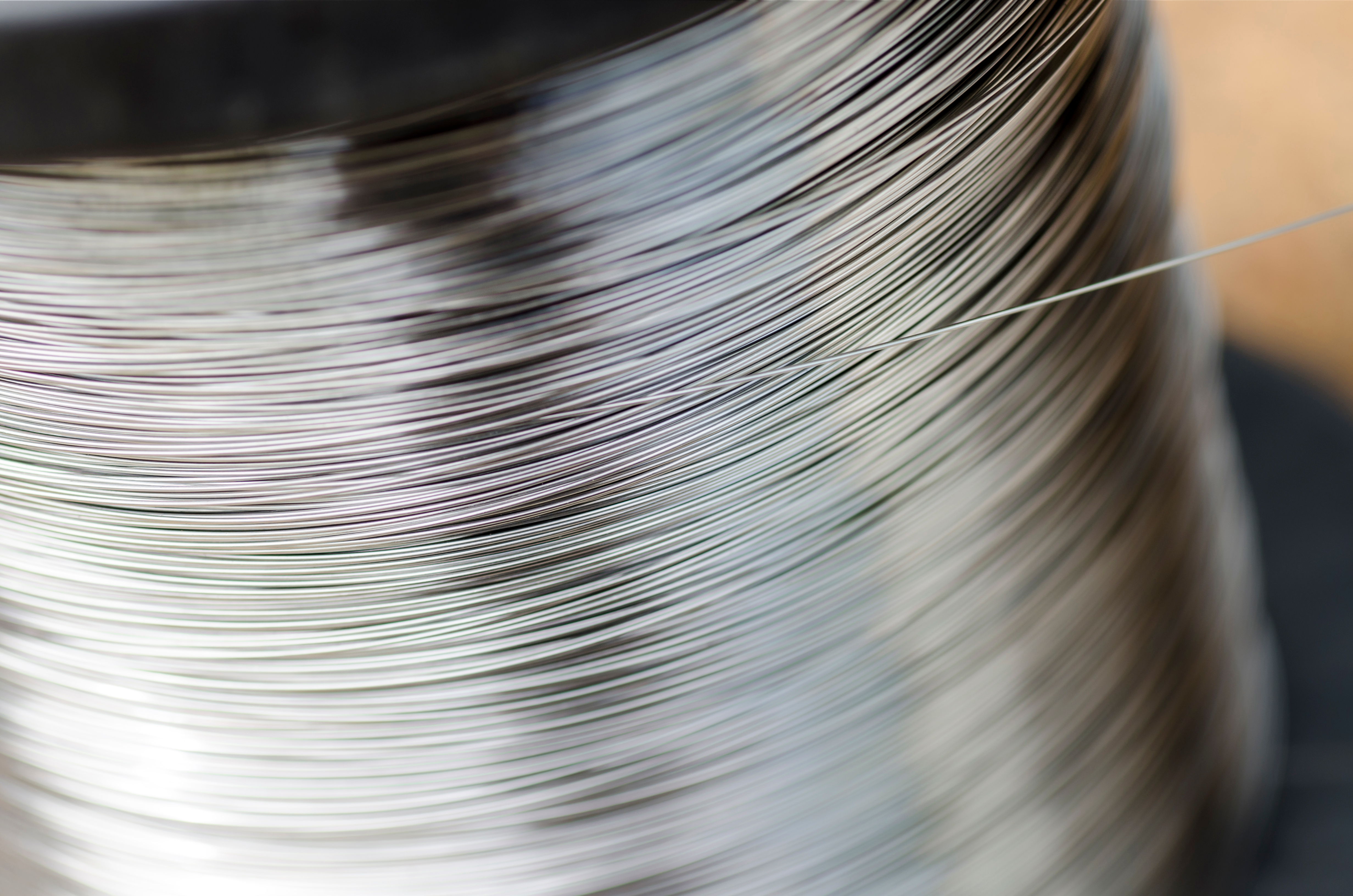 Nahaufnahme einer sich drehenden Spule mit glänzendem Metallfaden. Die verschwommene Bewegung erzeugt ein dynamisches und strukturiertes Muster.