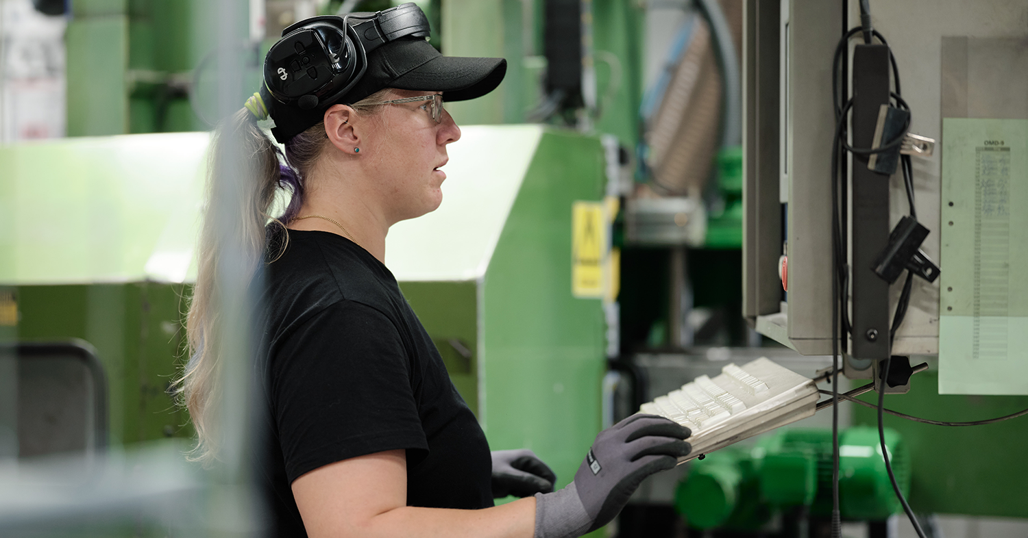 Eine Person mit schwarzer Kappe und Schutzbrille bedient Maschinen in einer industriellen Umgebung.