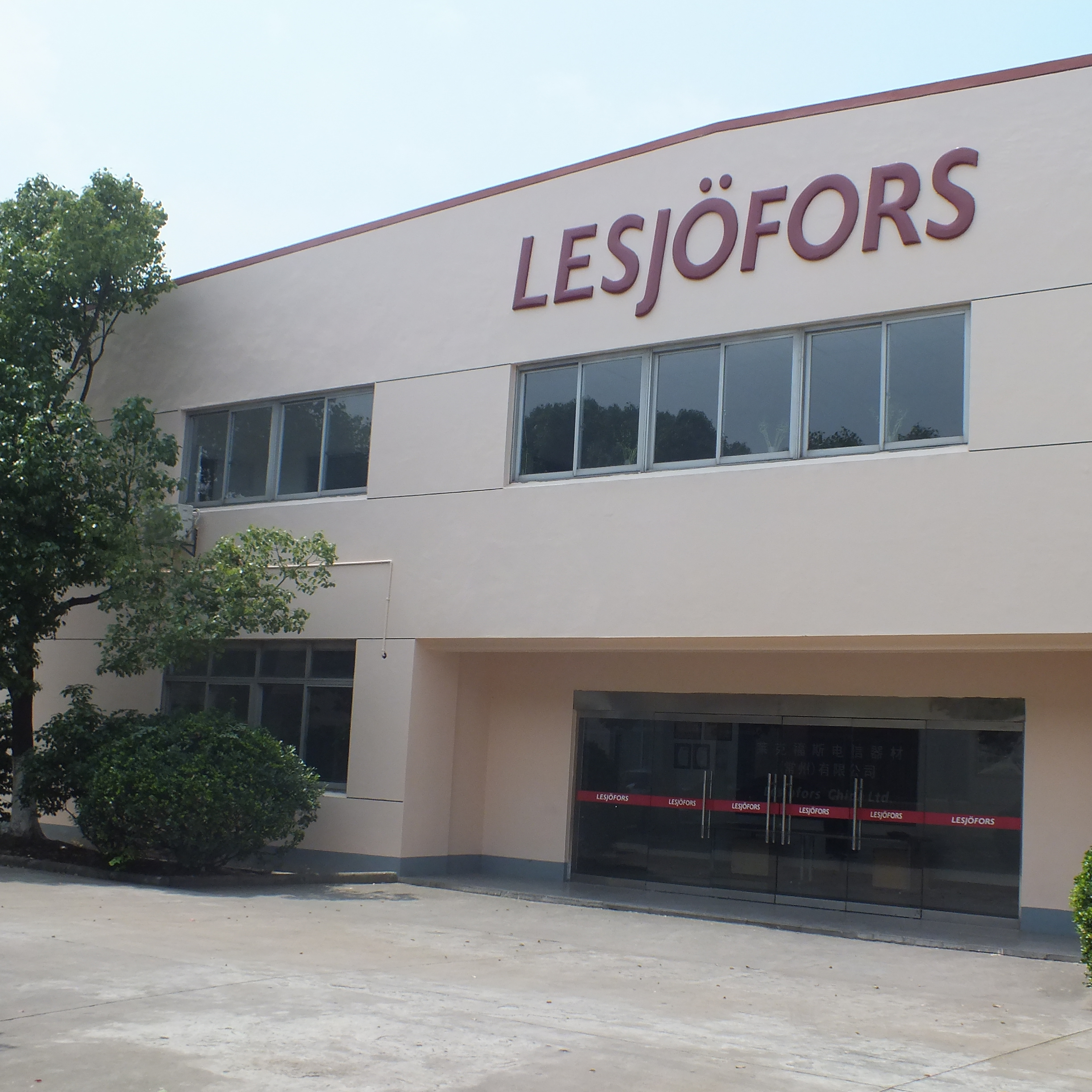 Skats no priekšpuses uz bēšu ēku ar lieliem logiem un uzrakstu “LESJÖFORS” augšpusē. Stikla durvis pie ieejas, ko ieskauj zaļumi.