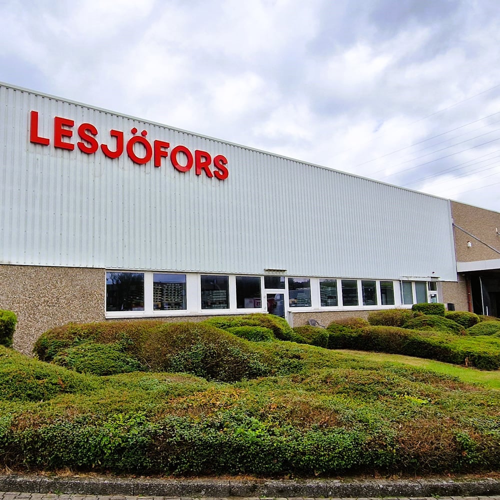 Exterior of the Lesjöfors manufacturing facility in Hagen, Germany, featuring the red Lesjöfors logo on the façade and well-maintained shrubs in front of the building.
