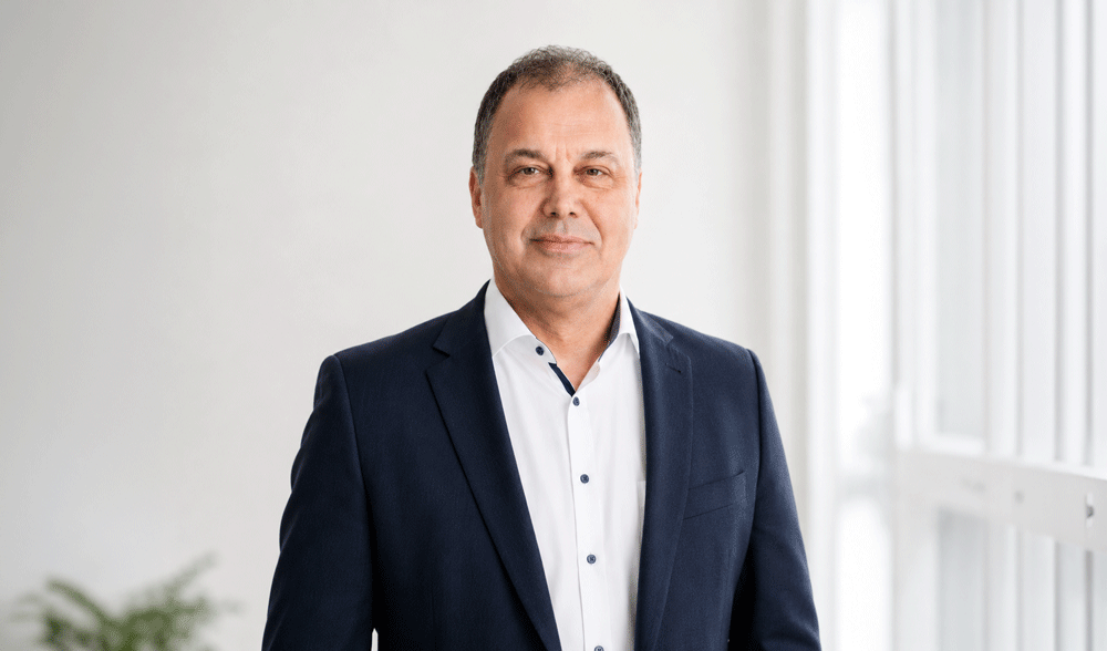 Horst Schillians, Managing Director, wearing a suit in front of a modern office background.